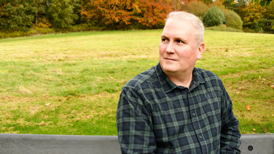 A photo of veteran Lee sat on a bench with an autumnal backdrop