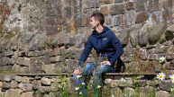 Veteran Steven sitting on a stone wall looking away
